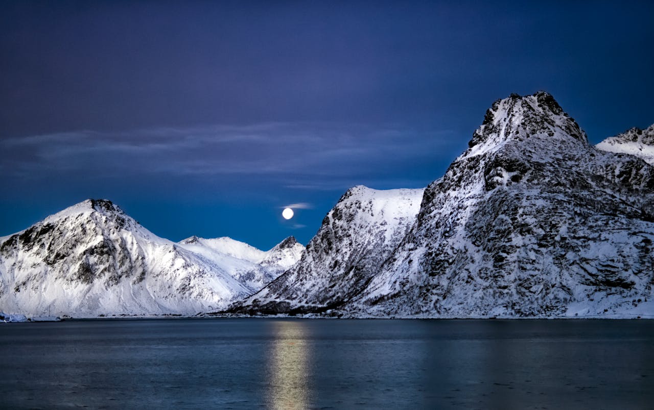 Stunning view of snowy mountains under a moonlit sky in Lofoten, Norway.